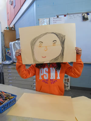A student holding up a drawing of a face.